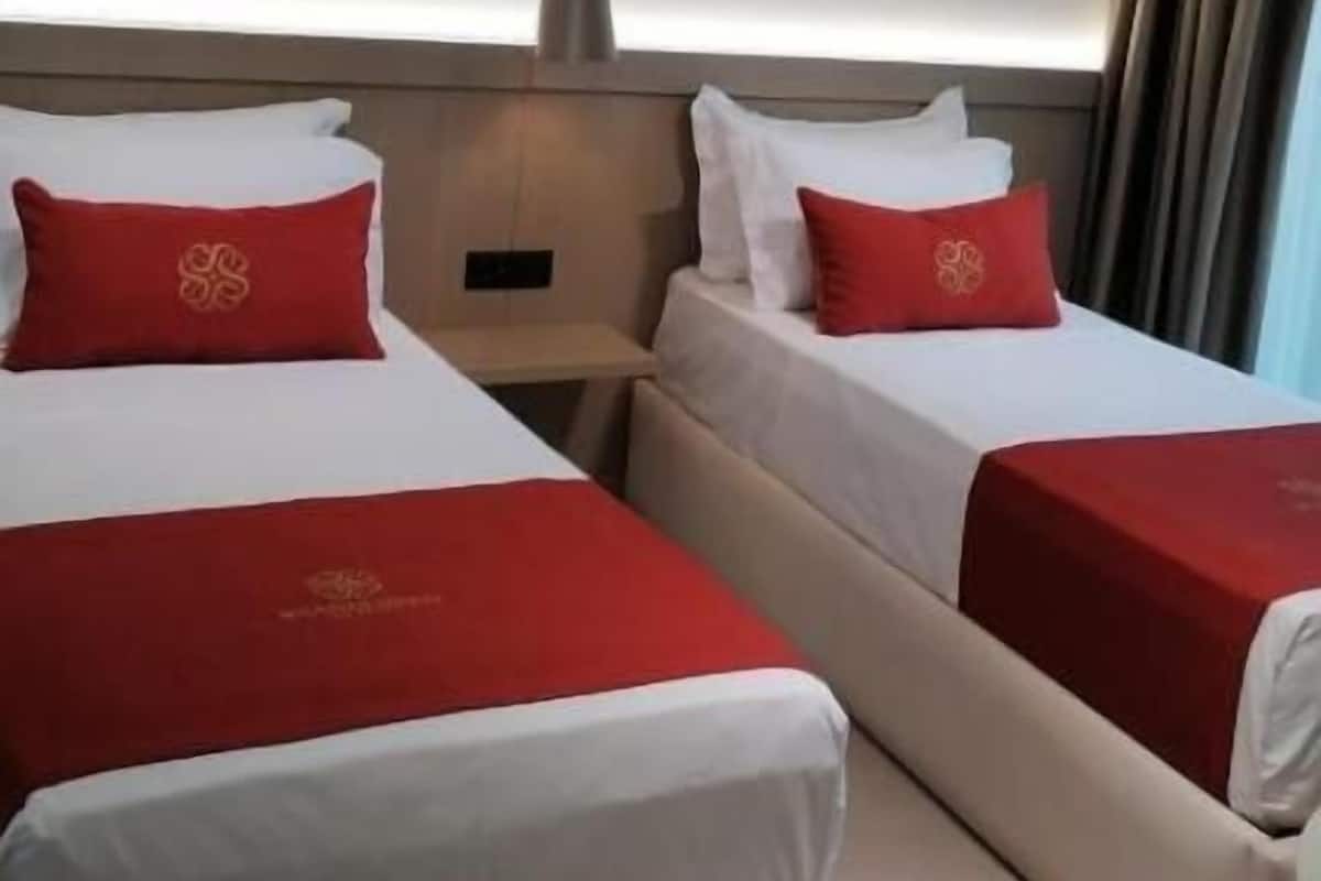 A hotel room with two beds, each with a red bedspread and matching pillows. There is a small table between the beds, and a ceiling light fixture above.