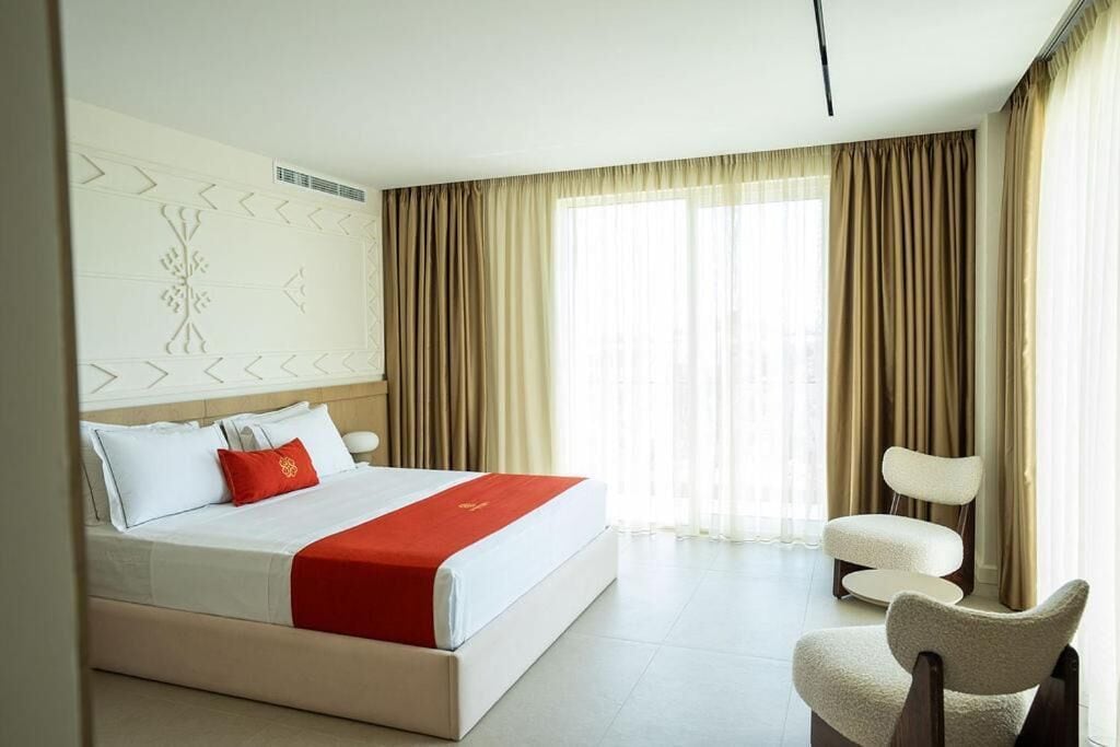 A hotel room with a large bed, a chair, and a window with curtains.