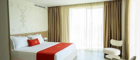 A hotel room with a large bed, a chair, and a window with curtains.