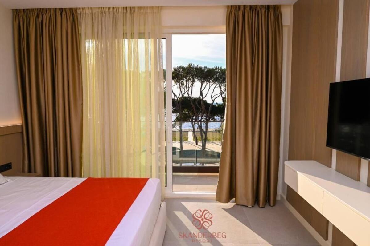A hotel room with a bed, a TV, and a balcony with curtains.