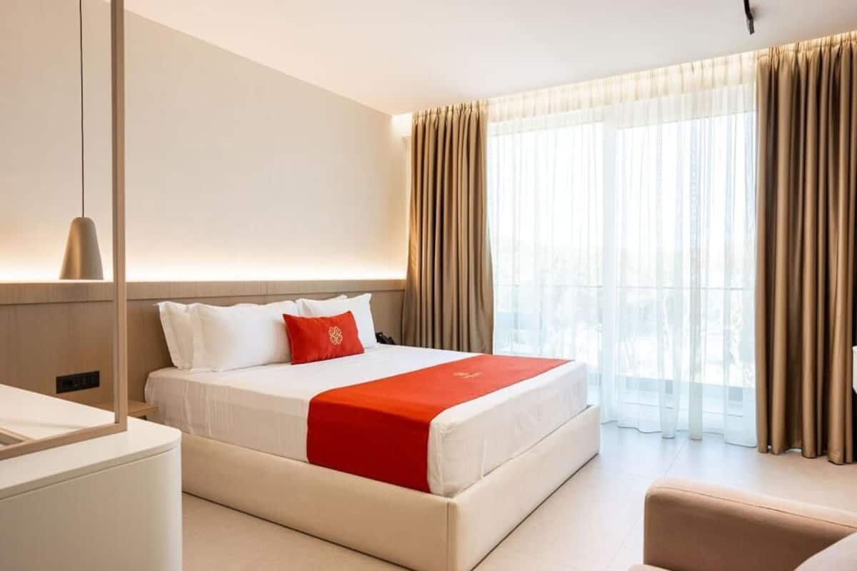 A hotel room with a bed, a bedside table, a lamp, and a window with curtains.