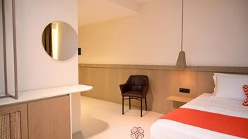 Quarto de hotel moderno com cama, uma cadeira, mesa de cabeceira, espelho e luminária fixada na parede.