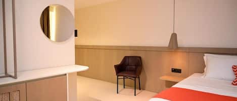 Habitación de hotel moderna con una cama, una silla, una mesita de noche, un espejo y una lámpara fijada a la pared.