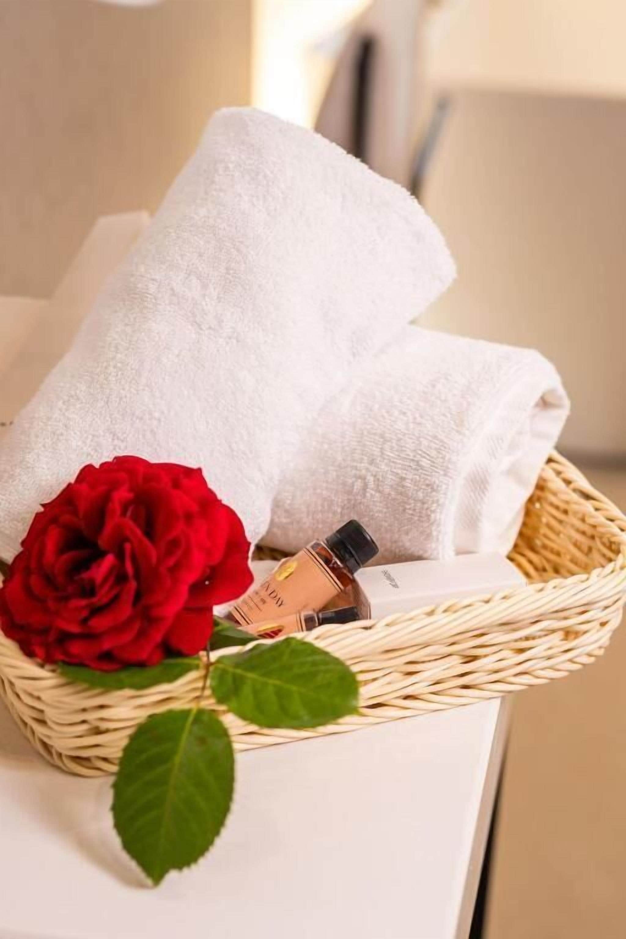 Una toalla blanca, una rosa roja y una botella de perfume en una cesta de mimbre.