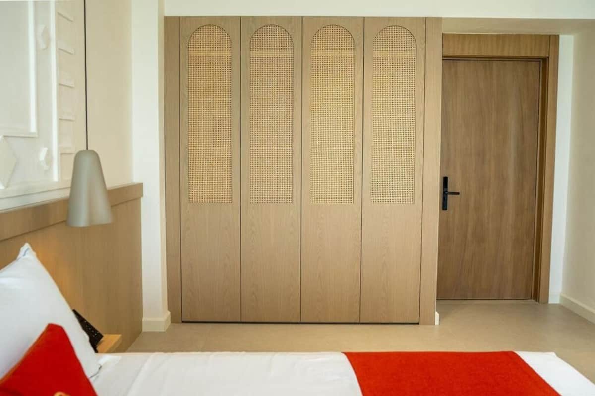 A hotel room with a bed, a red and white bedspread, a wooden wardrobe with a unique design, and a door.