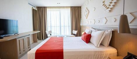 A hotel room with a large bed, a desk with a television, a phone, and a window with curtains.