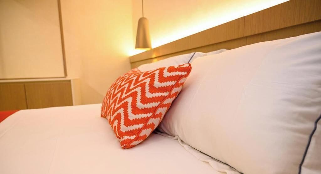 Una cama con ropa blanca y una única almohada de diseño rojo y blanco.