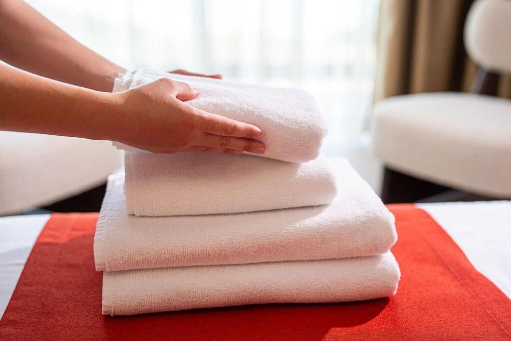 A stack of white towels on a red mat in a hotel room.