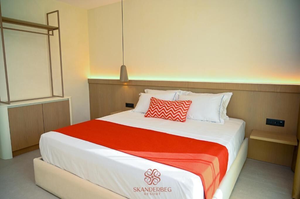 A hotel room with a bed, a nightstand, a wall-mounted shelf, and a pendant light.