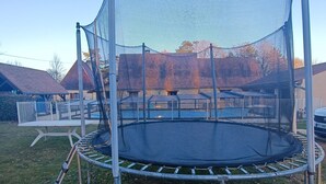 A trampoline with a safety net, surrounded by a metal frame, set on a grassy area with a fence in the background. - Charming Holiday Home in Journiac with Pool Access (Journiac)