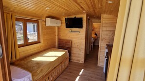 A cozy cabin interior with a wooden floor, a bed, a TV mounted on the wall, and a small kitchen area. - Charming Holiday Home in Journiac with Pool Access (Journiac)