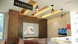 A reception area with a wooden panel wall, a reception desk, and a television mounted on the wall. - Sudev Residency (Mangaluru)