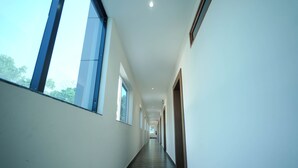 A long, narrow hallway with large windows on one side and doors on the other. - Sudev Residency (Mangaluru)