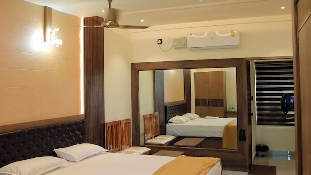 A hotel room with a large bed, a ceiling fan, an air conditioning unit, and a mirror reflecting the room. - Sudev Residency (Mangaluru)