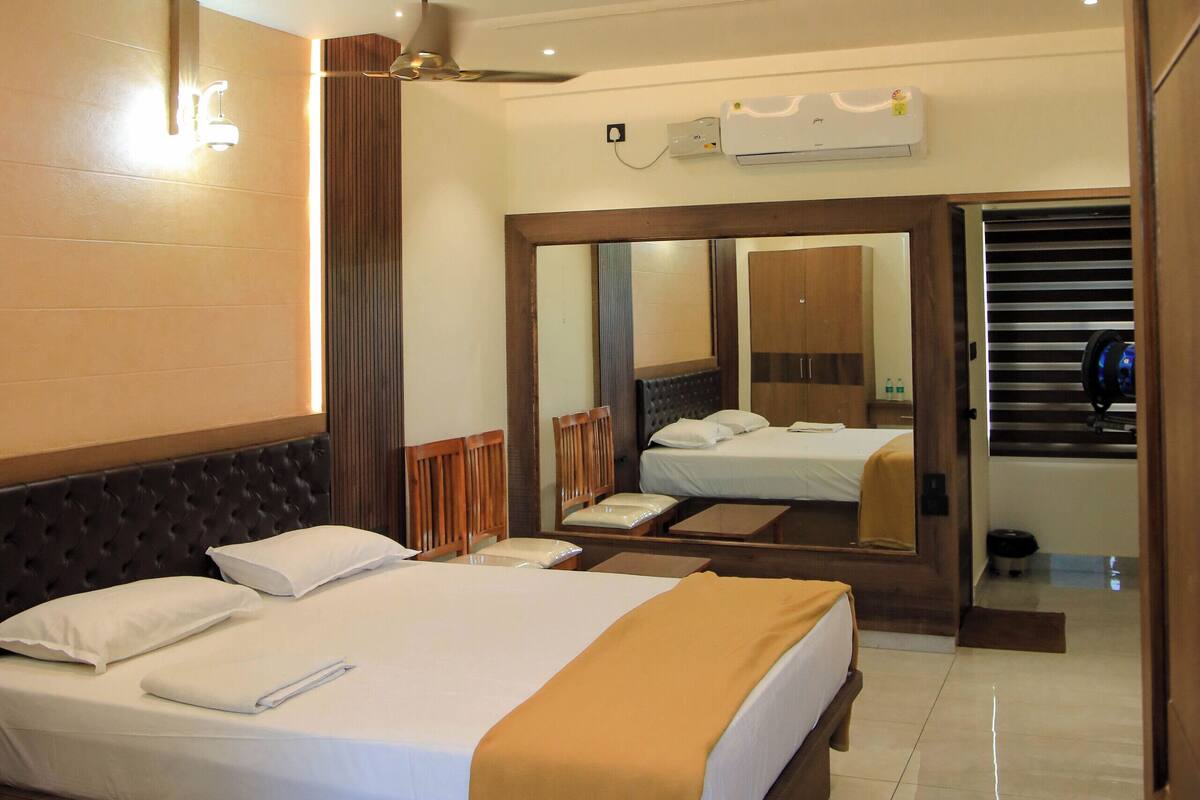 A hotel room with a large bed, a ceiling fan, an air conditioning unit, and a mirror reflecting the room.
