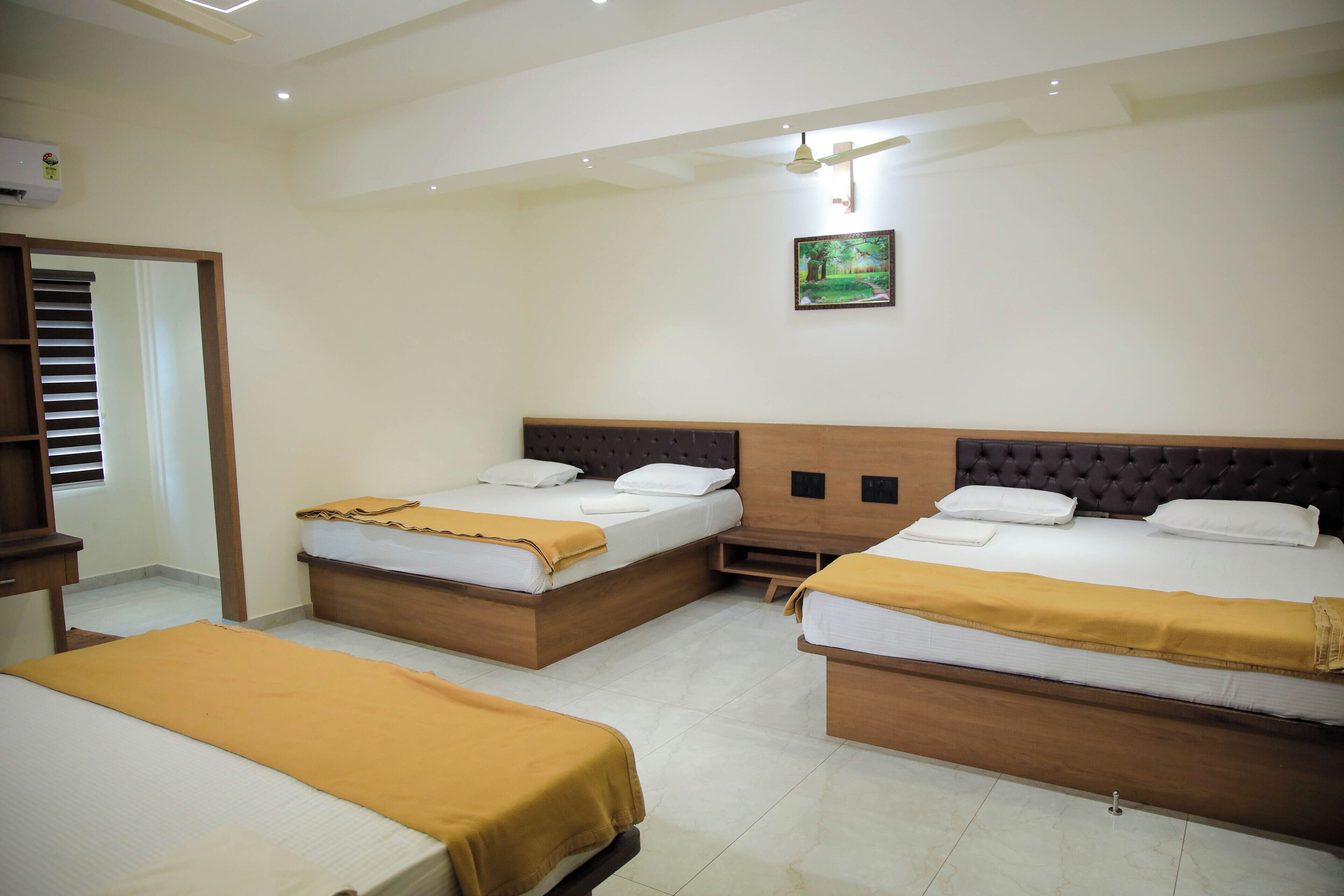 Una habitación de hotel con tres camas, cada una con cabecero de madera y ropa de cama blanca. Hay una mesita de noche de madera entre las camas, y un cuadro en la pared sobre ellas.