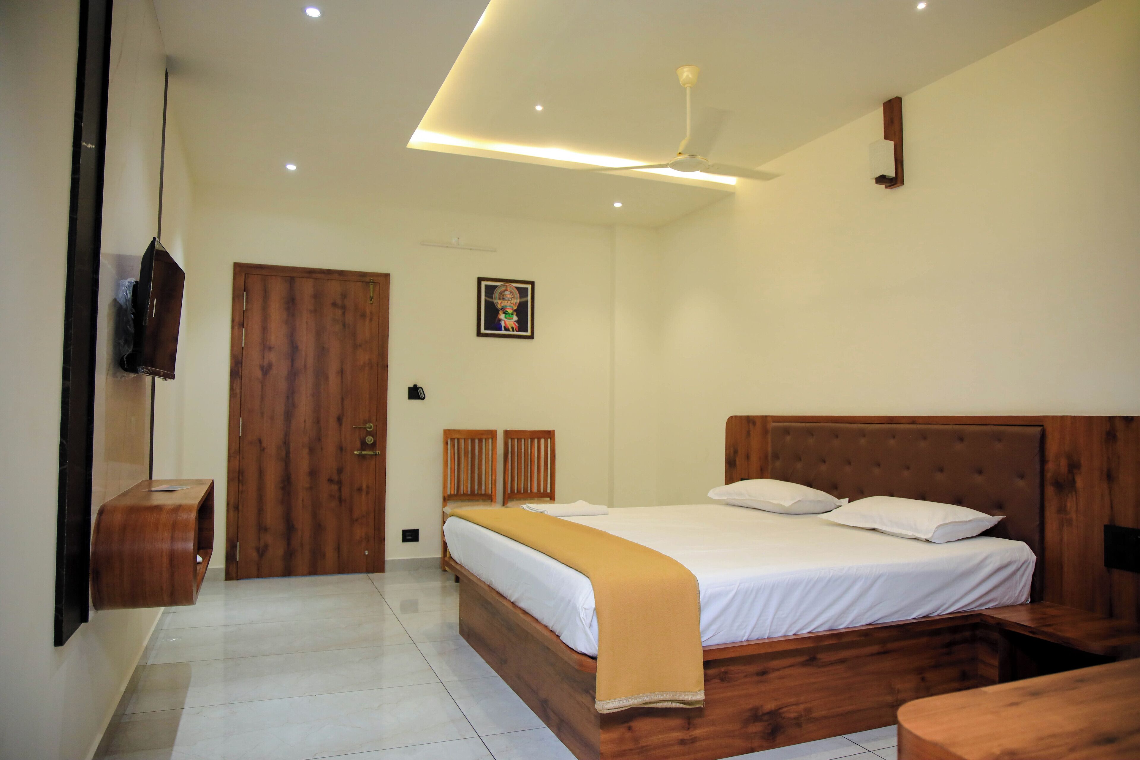 Une chambre à coucher avec un lit en bois, une table de chevet, un ventilateur de plafond et un téléviseur fixé au mur.