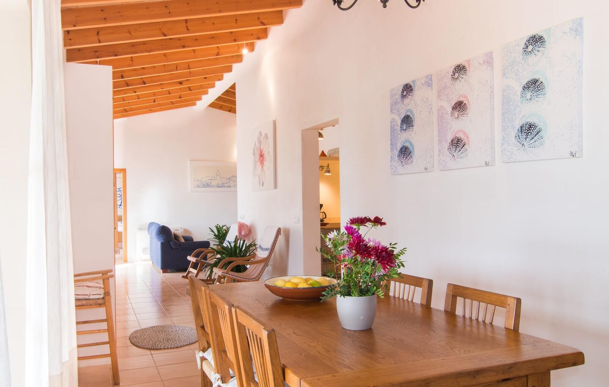 A dining area with a wooden table, chairs, a bowl of fruit, and a potted plant.