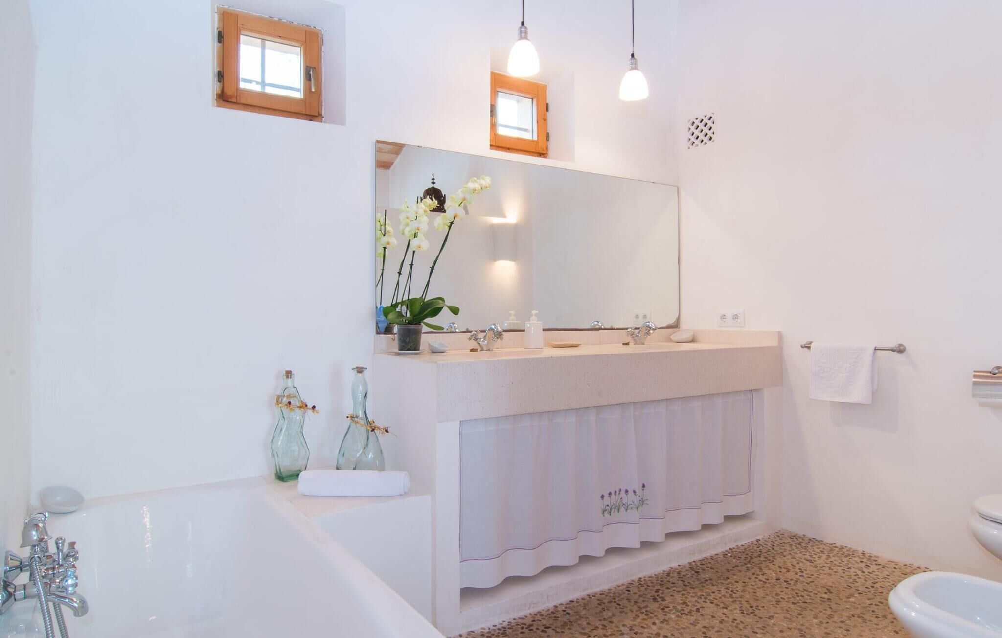 Un baño moderno con una bañera, un lavamanos con espejo y un inodoro. Hay dos ventanas pequeñas y una lámpara en el techo.