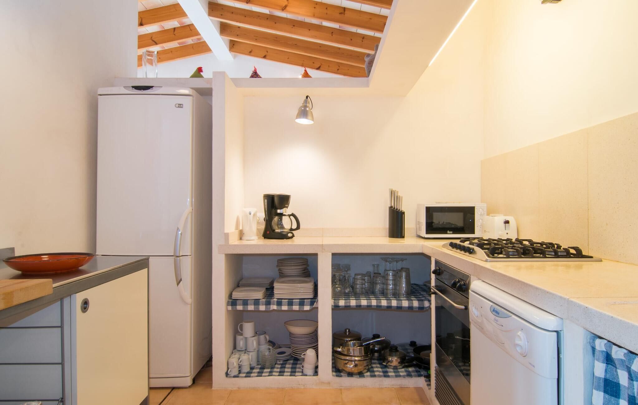 Eine kleine Küche mit Kühlschrank, Mikrowelle, Herd und Regalen mit Geschirr und Besteck.