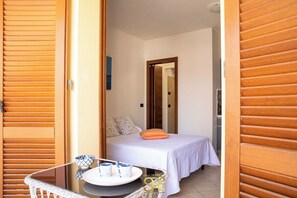 A compact bedroom with a bed, a small table with a tray of cups and a plate, and a wooden door. - Alghero center Charme 1 (Alghero)