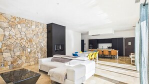 A modern living room with a stone wall, a sofa, a coffee table, and a kitchen in the background. - VILLA PROVENÇALE AVEC PISCINE (Montauroux)