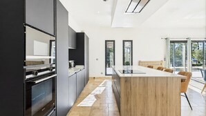 A modern kitchen with a central island, black cabinetry, and a large window. - VILLA PROVENÇALE AVEC PISCINE (Montauroux)