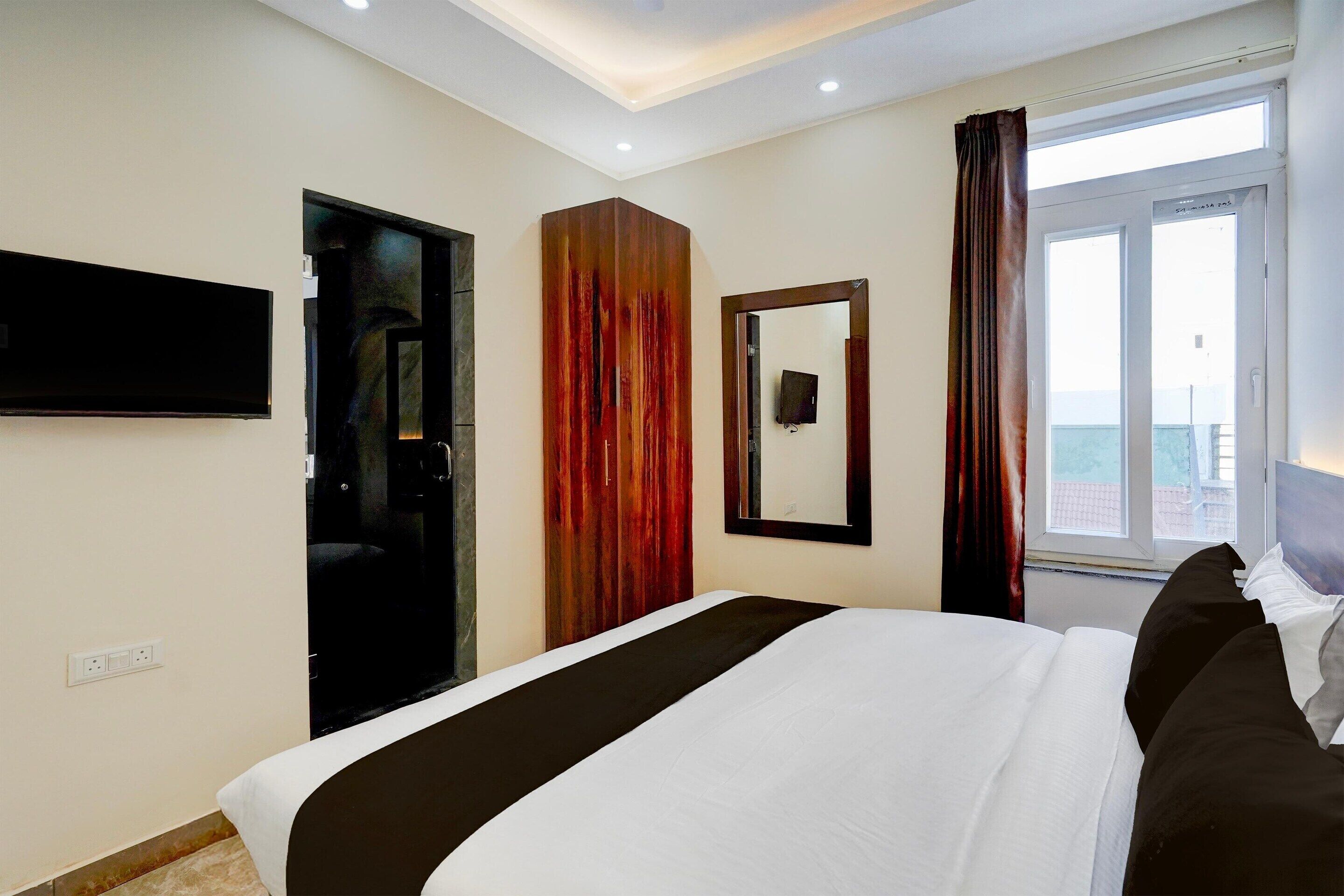 Een hotelkamer met een groot bed, een aan de muur bevestigde televisie, een spiegel en een raam met gordijnen.