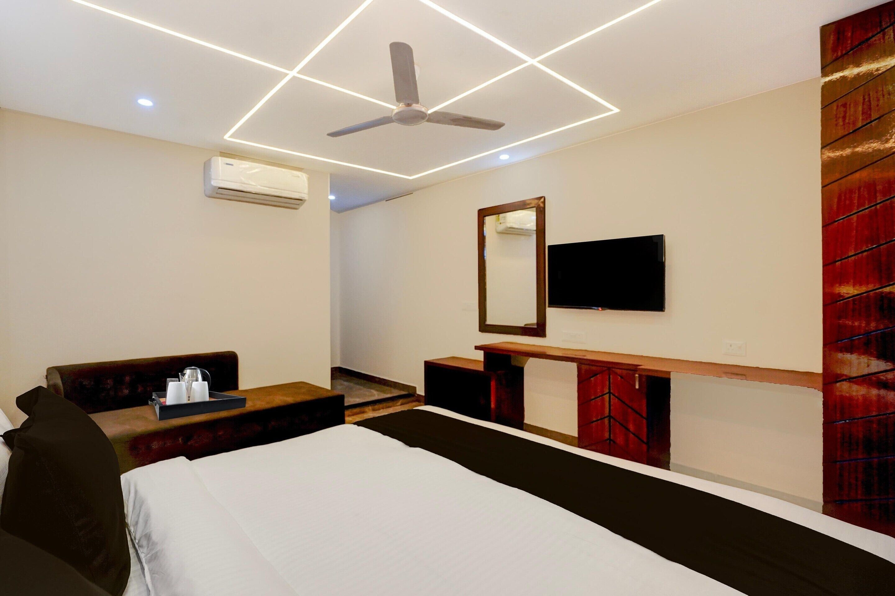 A hotel room with a bed, a seating area with a sofa and a small table, a TV mounted on the wall, and a ceiling fan.
