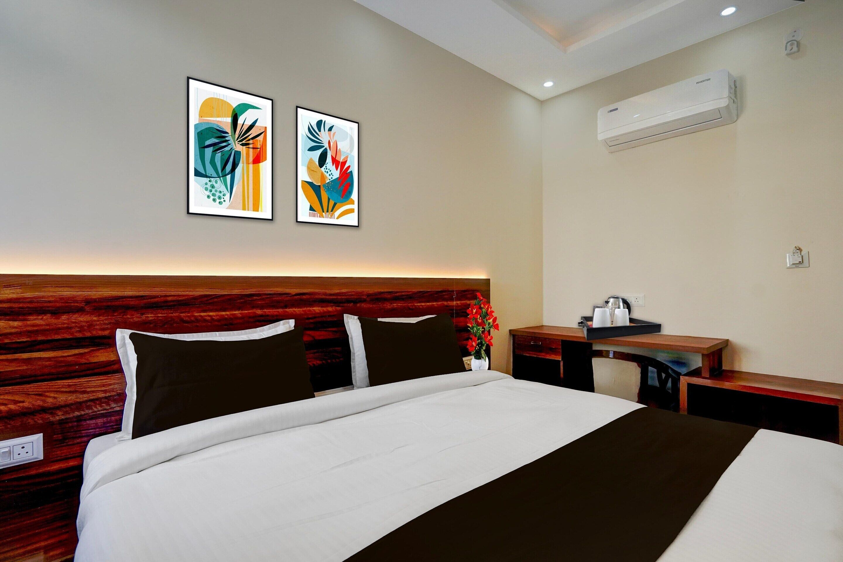 A hotel room with a bed, a nightstand, a desk, an air conditioner, and two wall-mounted artworks.