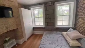 Ein Schlafzimmer mit einem Bett, zwei Fenstern, einem Fernseher und einem Kleiderschrank.