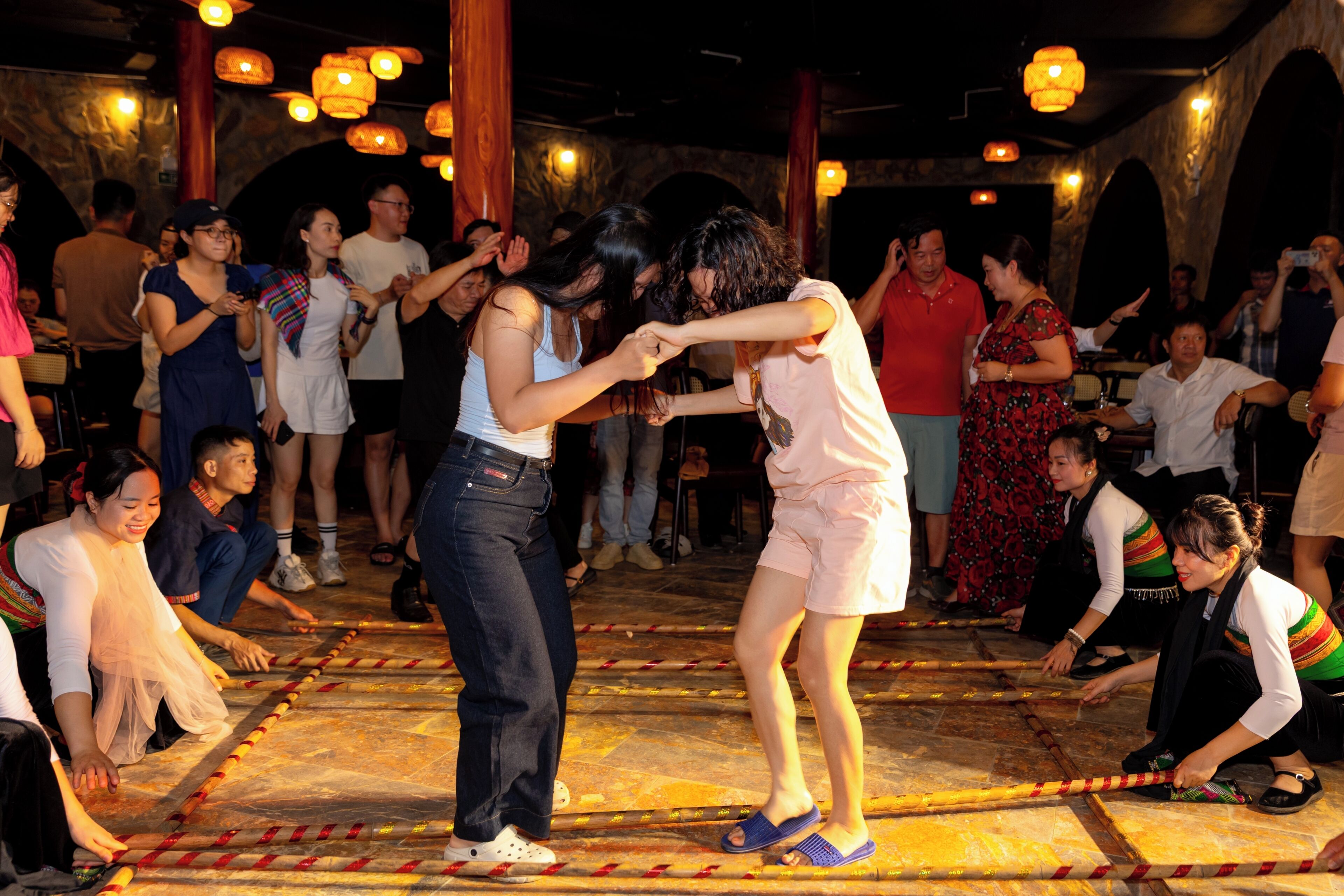 A group of people participating in a traditional dance on a patterned floor, with onlookers seated around.
