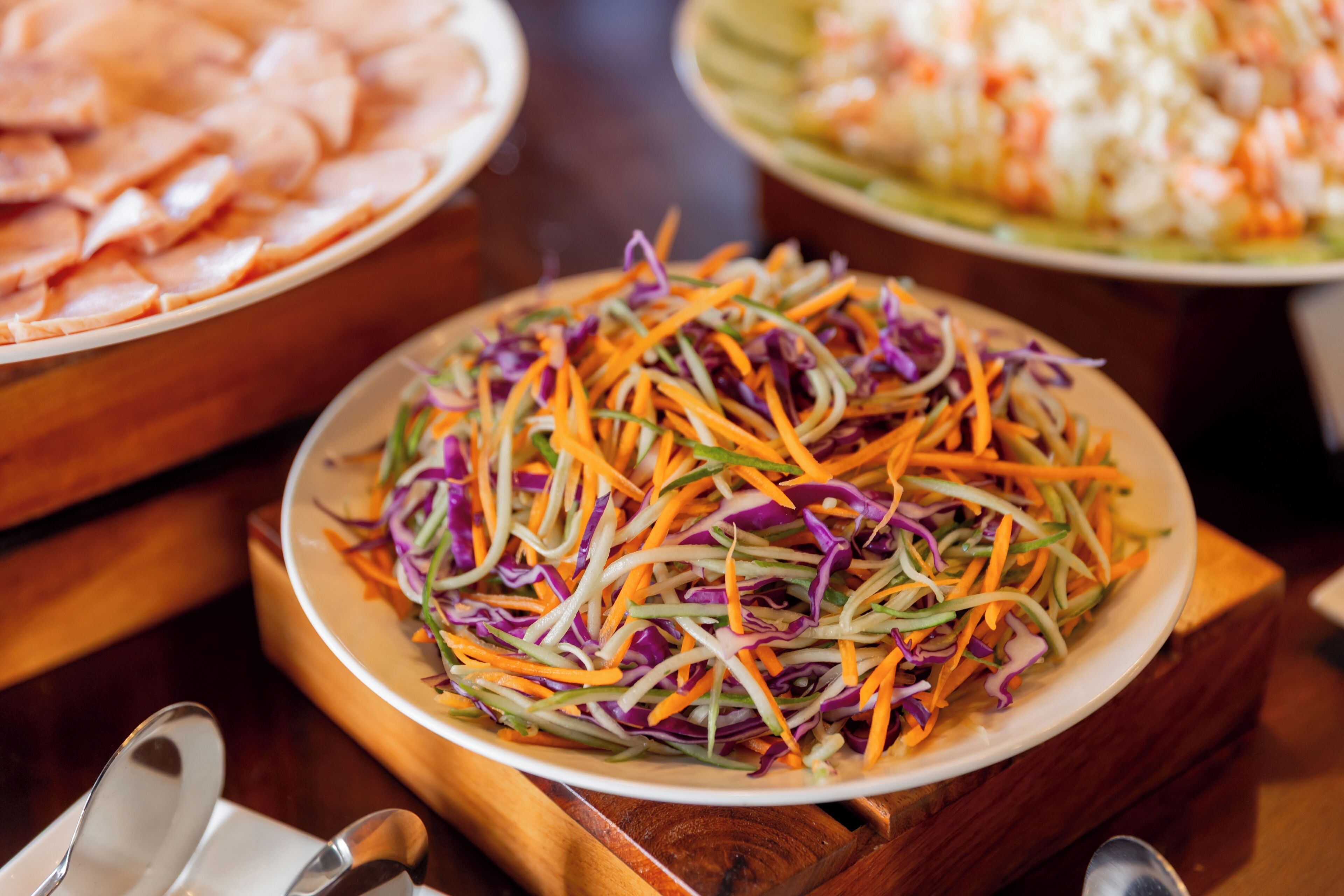 Diversos pratos sobre uma mesa, incluindo um prato de carne fatiada e uma salada colorida.