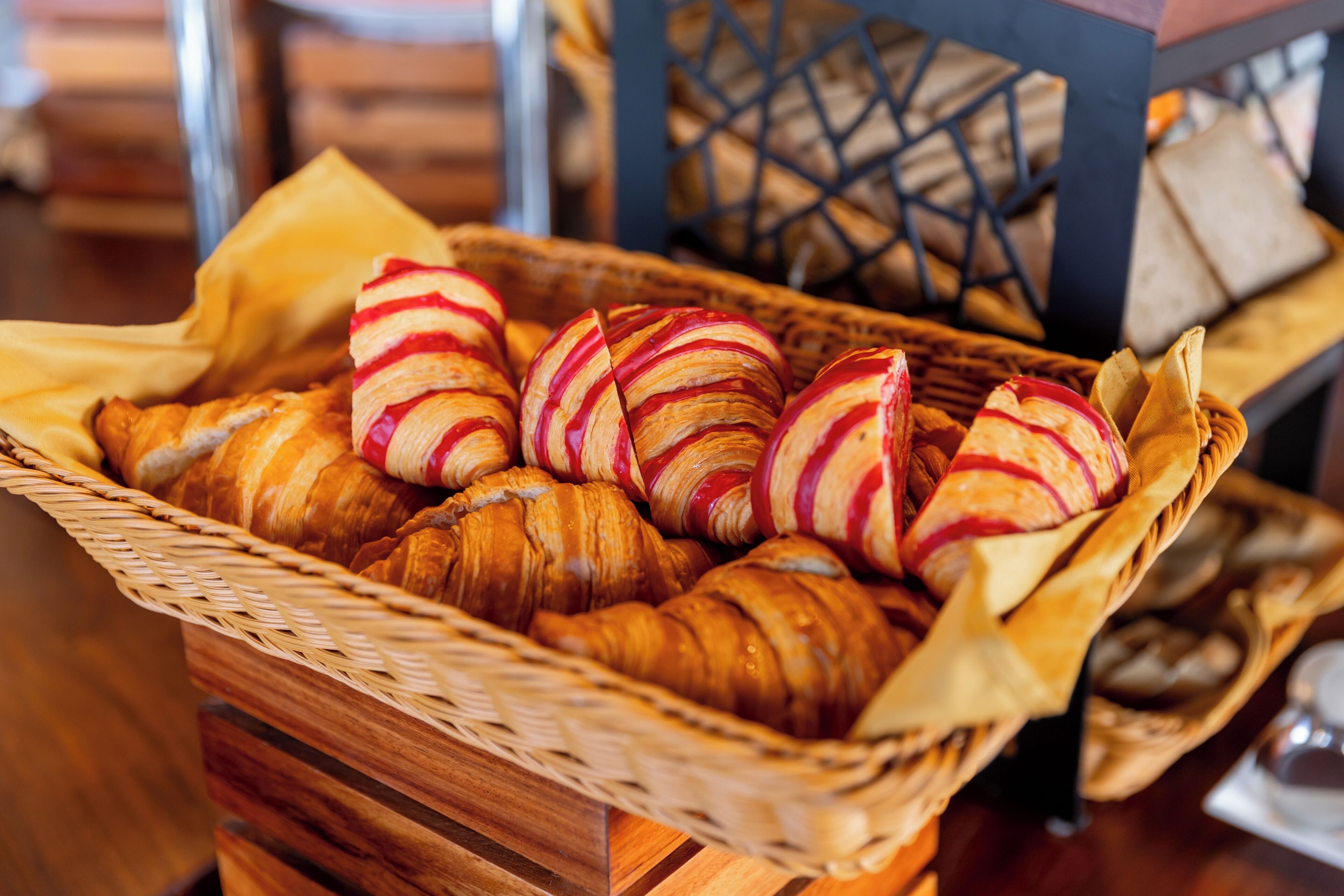 A basket of croissants and bread on a wooden table.