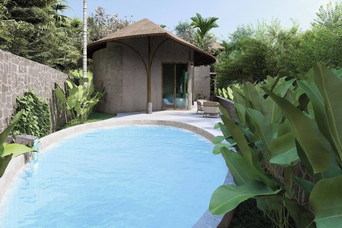 A swimming pool with a stone wall, a small building with a thatched roof, and lush tropical plants.