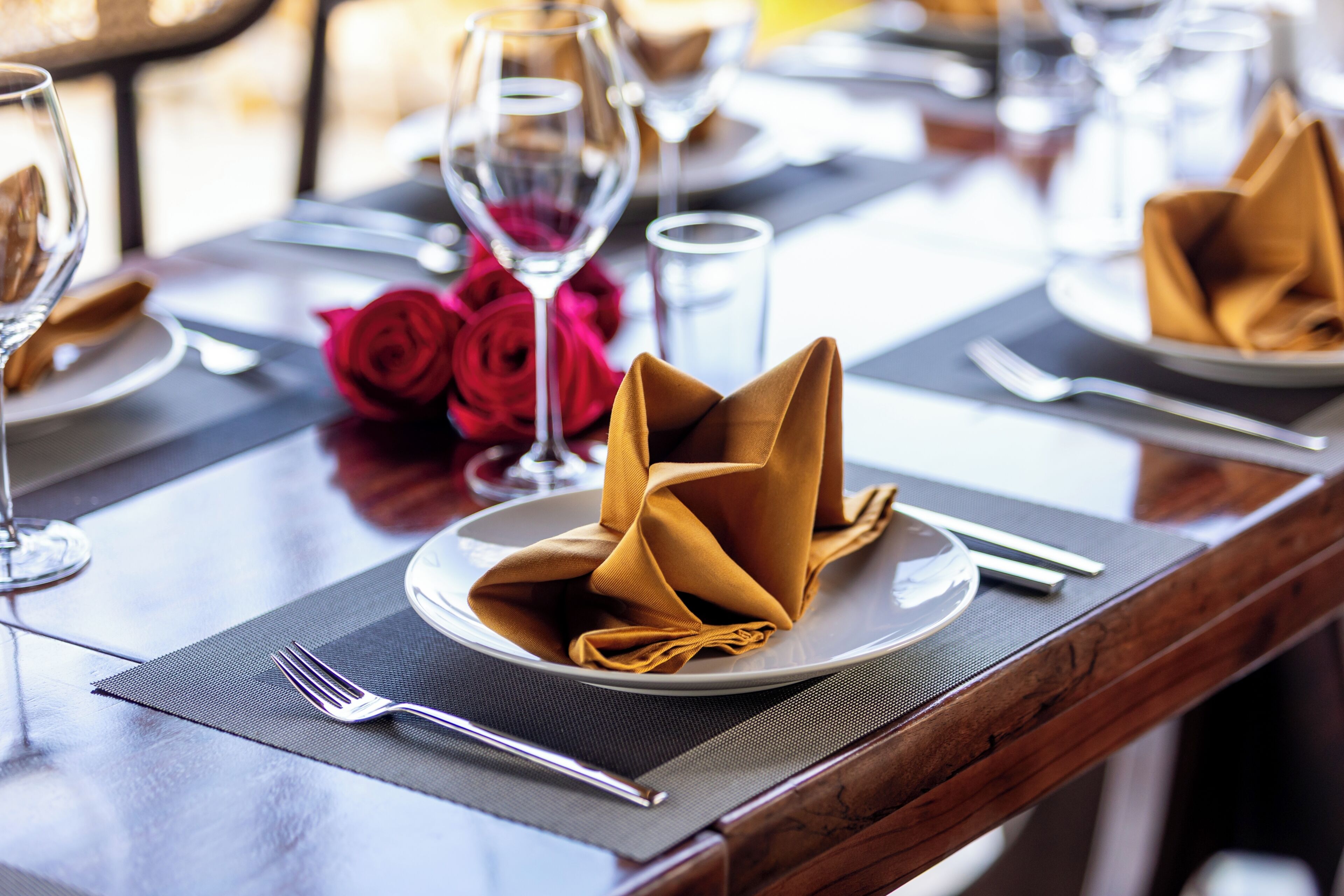 A dining table with a folded napkin, a fork, a glass, and a red rose.