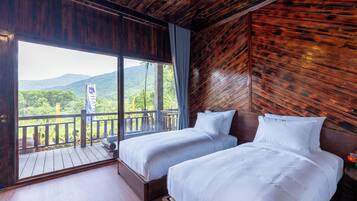 Una habitación con dos camas, un balcón con barandilla de madera y vistas a zonas verdes y montañas.