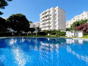 A swimming pool with a clear blue surface, surrounded by greenery and a multi-story building with balconies. - Seaview Retreat Apartment with Pool REF067 (Benalmádena)