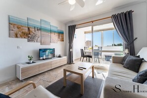 Ein modernes Wohnzimmer mit Flachbildfernseher, Couch, Holztisch und einem Essbereich mit Tisch und Stühlen.