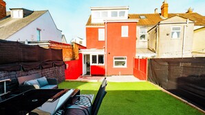 A backyard with artificial grass, a barbecue area, and a red building.