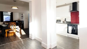 A modern kitchen with white cabinets, a red accent wall, and a dining area with wooden chairs and a table.
