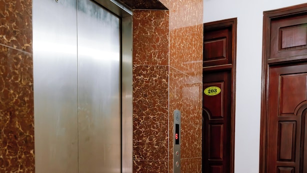 Egy digitális kijelzővel, márványfalakkal és egy fával borított ajtóval ellátott lift, melynek felett egy tábla található.