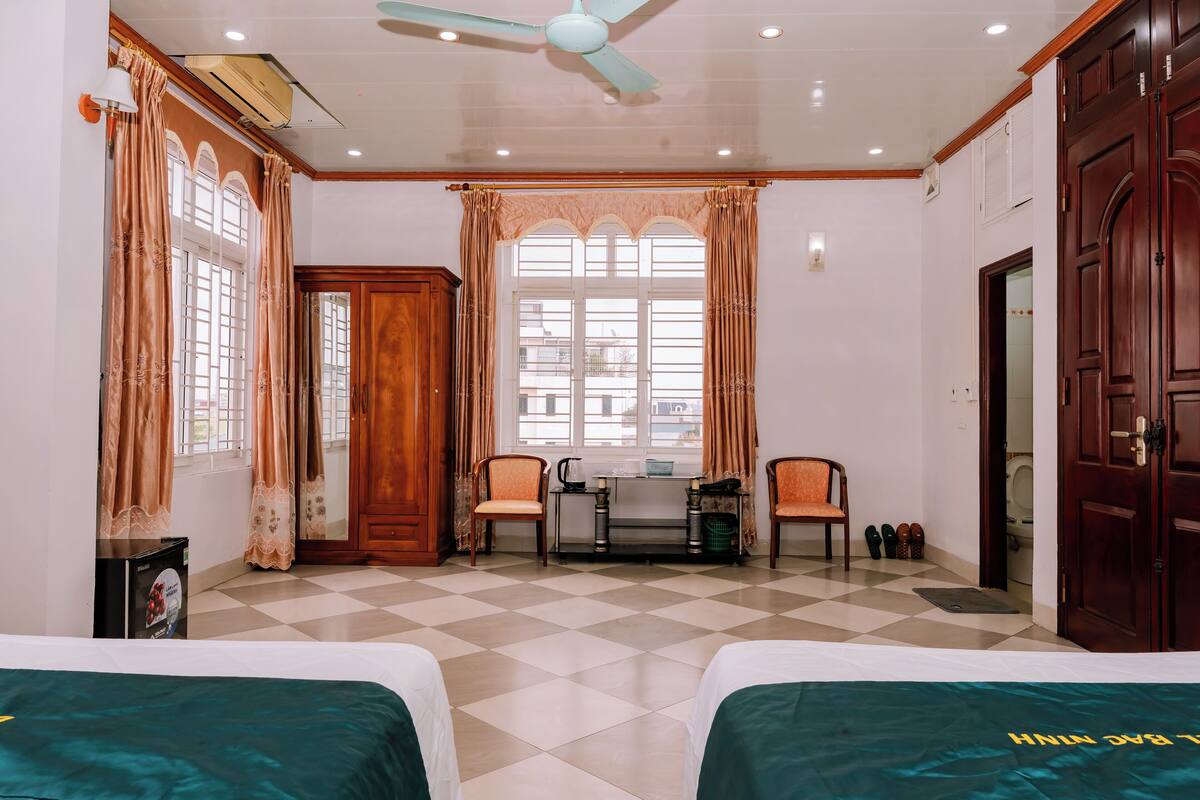 Habitación de hotel con dos camas, un escritorio, sillas, un ventilador de techo y una ventana con cortinas.