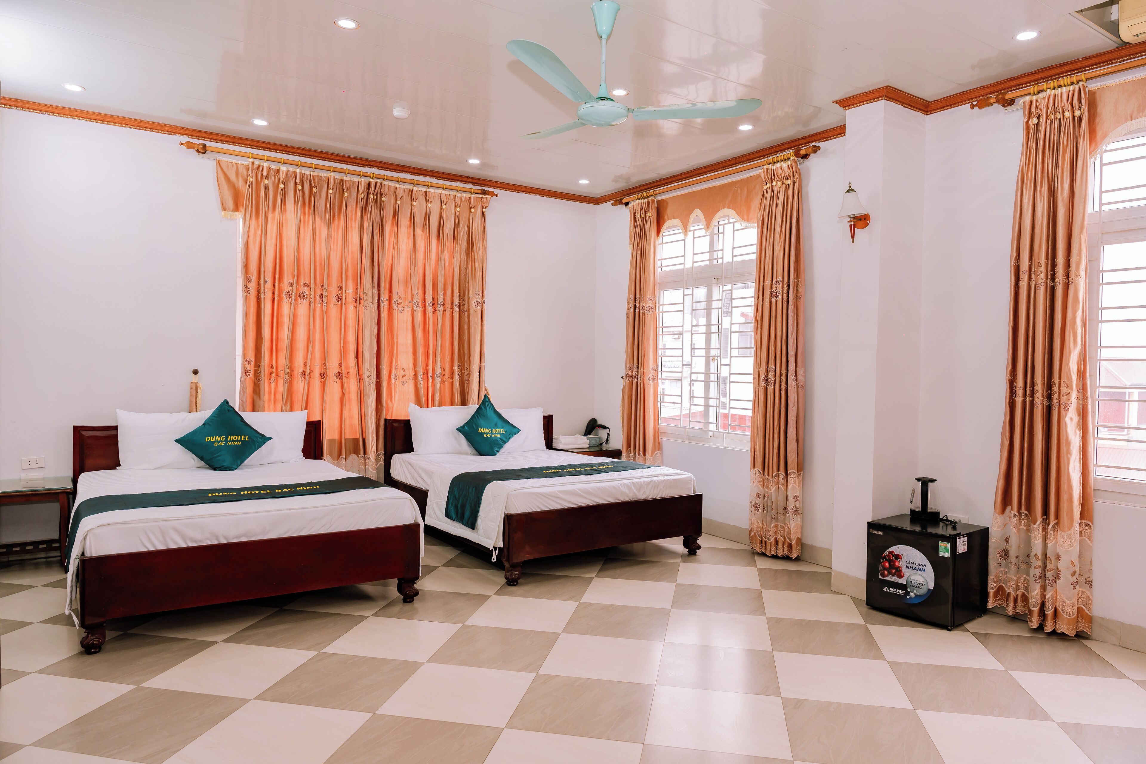A hotel room with two beds, a ceiling fan, and a minibar.