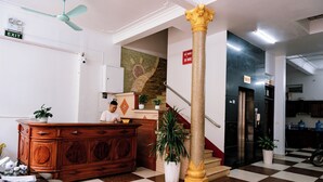 Egy előtér, amelynek a padlója kockás mintájú, egy recepciós pult, egy lépcsőház és egy oszlop található benne.