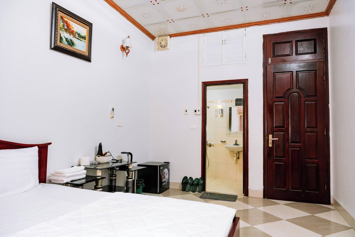 Habitación de hotel con cama, escritorio con tetera, un cuadro en la pared y puerta de madera.