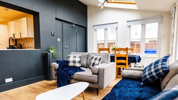 A modern living room with a grey sofa, a white coffee table, and a blue blanket. - Gloucester Kingsholm 6 Bedrooms (Gloucester)