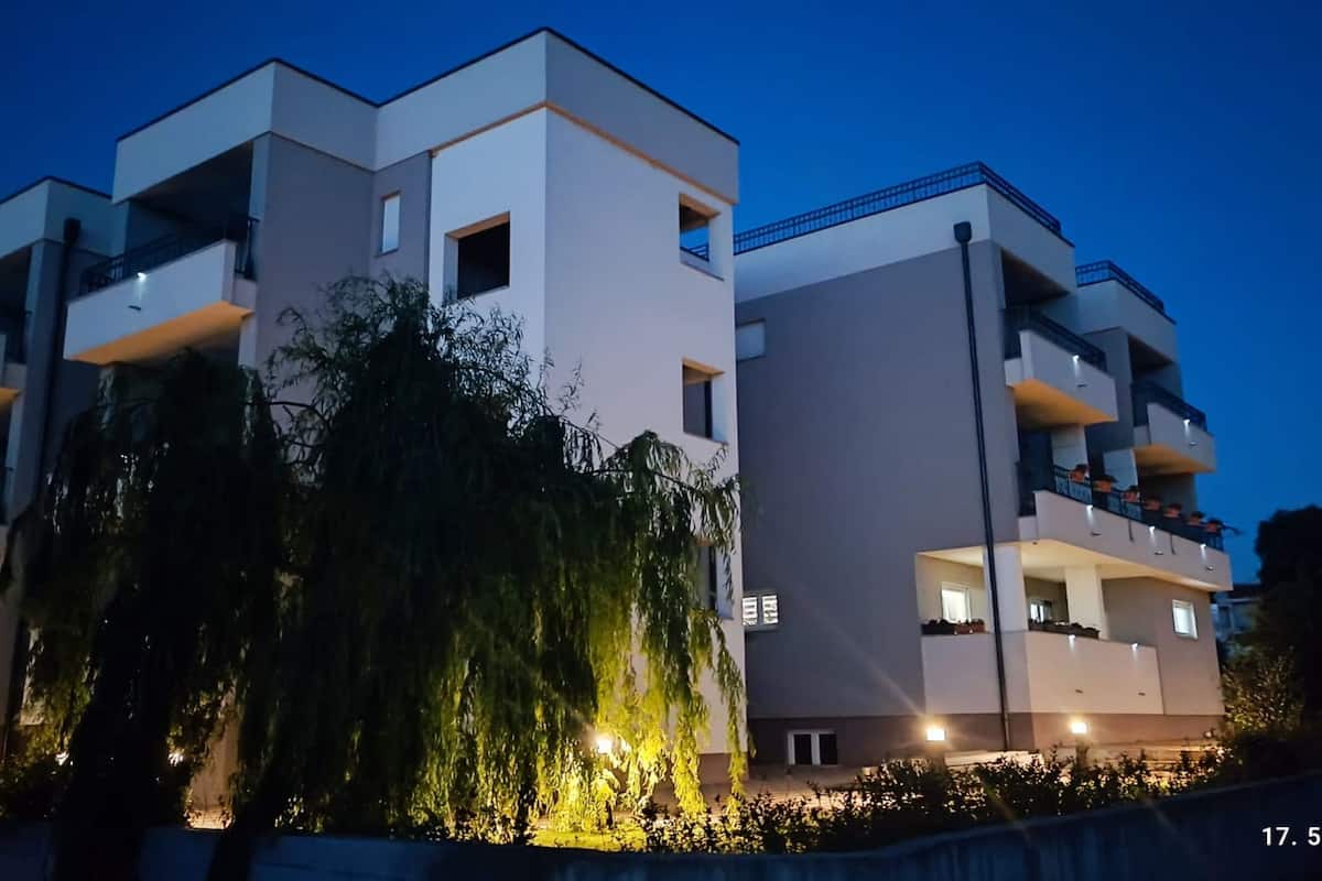 Un immeuble moderne à plusieurs étages, doté de balcons et agrémenté d’un élément décoratif aquatique à l’avant.
