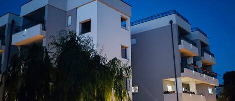 A modern multi-story building with balconies and a water feature in front.