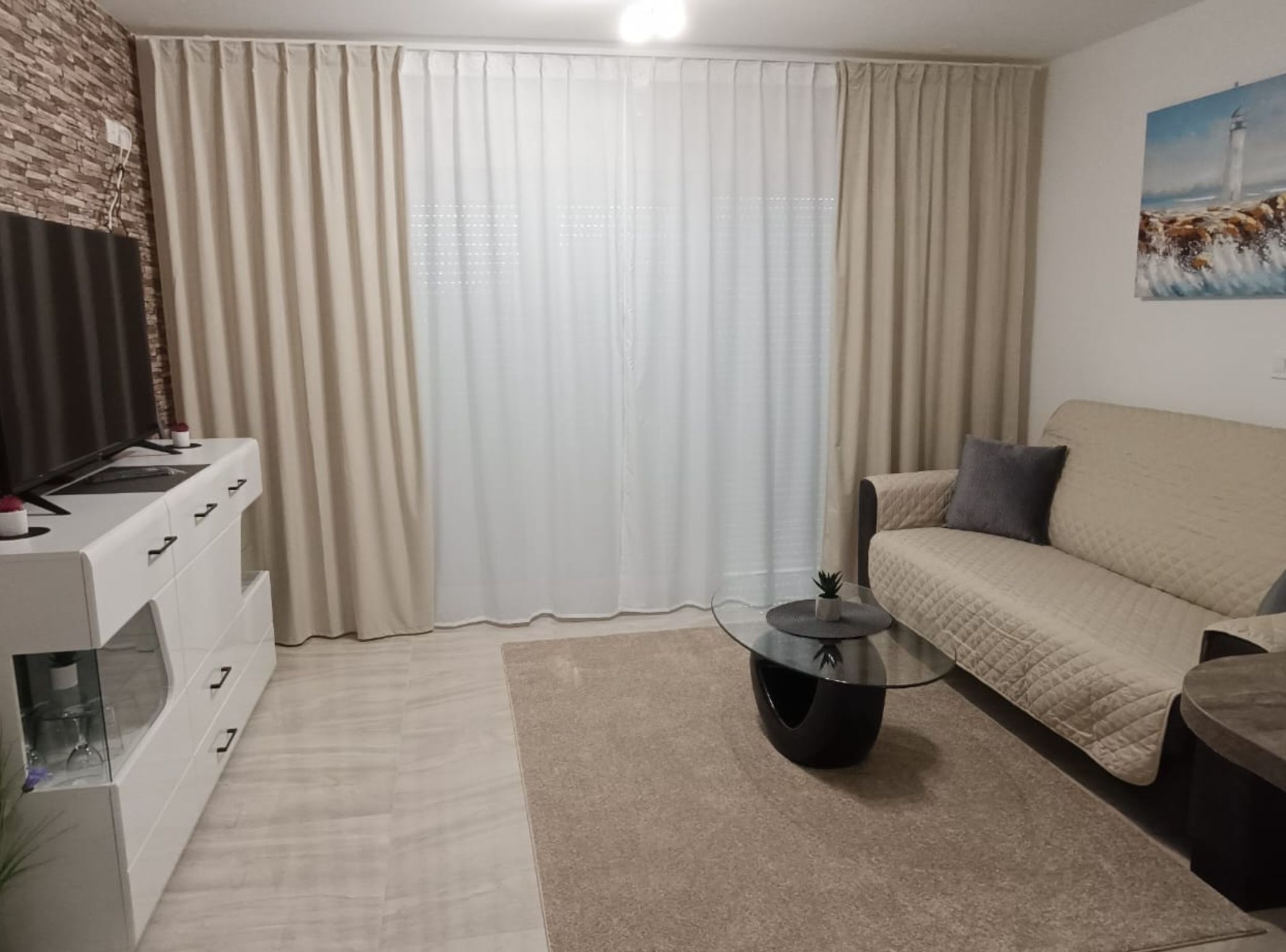 Una sala de estar moderna con un sofá, una mesa de centro de vidrio y un televisor sobre un mueble blanco.